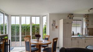 A dining area with a table and chairs, a kitchen with cabinets, and a sliding glass door leading to a garden. - Holiday Home 'Ferienhaus Beckerwitz' with Private Terrace, Garden & Wi-Fi (Beckerwitz)