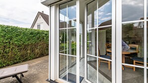A conservatory with glass doors, a bench, and a table with chairs inside. - Holiday Home 'Ferienhaus Beckerwitz' with Private Terrace, Garden & Wi-Fi (Beckerwitz)