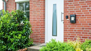 A red brick building with a white door, a mailbox, and green foliage. - Holiday Home 'Ferienhaus Beckerwitz' with Private Terrace, Garden & Wi-Fi (Beckerwitz)