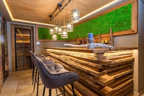 Uma área de bar com balcão de madeira, parede verde e luminárias pendentes.