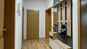 A hallway with wooden flooring, a wooden door, a white wall with a round ceiling light, and a wooden cabinet with a mirror and hooks. - Apartment 'Das Grüne Haus' with Shared Terrace and Shared Garden (Finsterwalde)