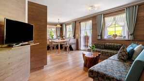 Una sala de estar moderna con un televisor de pantalla plana, piso de madera, una zona de comedor con mesa y sillas, y un sofá con cojines estampados.