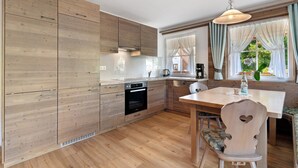 Una cocina con armarios de madera, una mesa de comedor y un ventanal con cortinas.