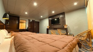 Ett hotellrum med en stor säng, en tv som är monterad på väggen, en sittgrupp med flätade stolar och ett tak med infälld belysning.