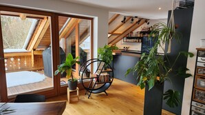 A modern interior with a wooden floor, a dining area, a black rocking chair, and a staircase with wooden beams.