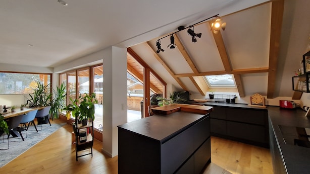 A modern kitchen with a central island, wooden beams, and large windows.