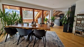 A modern dining area with a wooden table, black chairs, and potted plants.