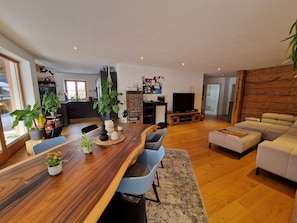 Ein modernes Wohnzimmer mit einem Holzespeisetisch, blauen Stühlen, einem beigen Sofa und einem Fernseher.