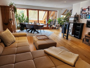 Ein modernes Wohnzimmer mit Sofa, Hocker und Essbereich mit Stühlen und Tisch.
