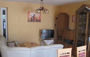 Una sala de estar con un sofá, un televisor, una mesa con un florero y un aparador con cristalería.