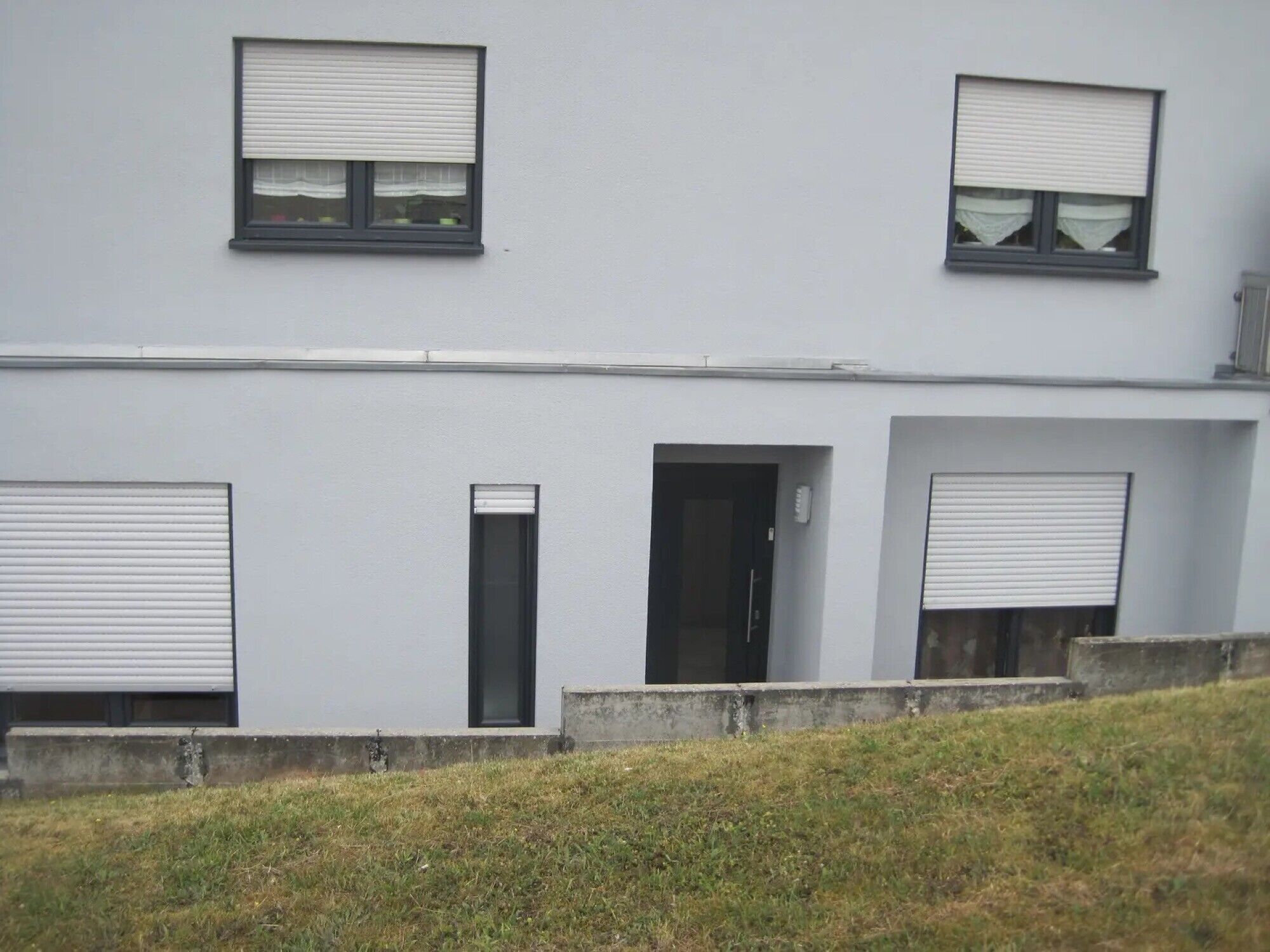 Un edificio moderno con tre finestre, un'entrata e due basculanti per garage.