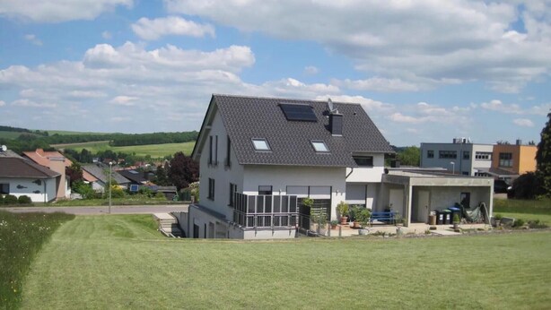 Une maison à deux étages, dotée d’un toit en pente, de panneaux solaires et d’un petit garage attenant.