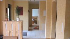 Un couloir avec un meuble, une plante en pot et une porte qui donne sur une pièce.