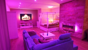 A modern living room with a TV, a fireplace, a four-poster bed, and a stone wall.