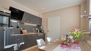 A modern kitchen with dark cabinets, a built-in oven, and a flat-screen TV. There is a dining table with a floral tablecloth and chairs.