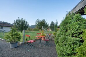 A patio with a table and chairs, surrounded by greenery and a fence.