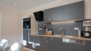 A modern kitchen with grey cabinets, a built-in oven, a dishwasher, and a coffee maker.