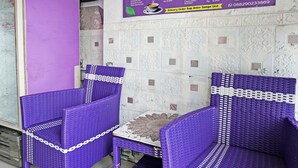 Due poltrone viola in vimini con un tavolino, una parete viola e una bacheca con il menu sullo sfondo.