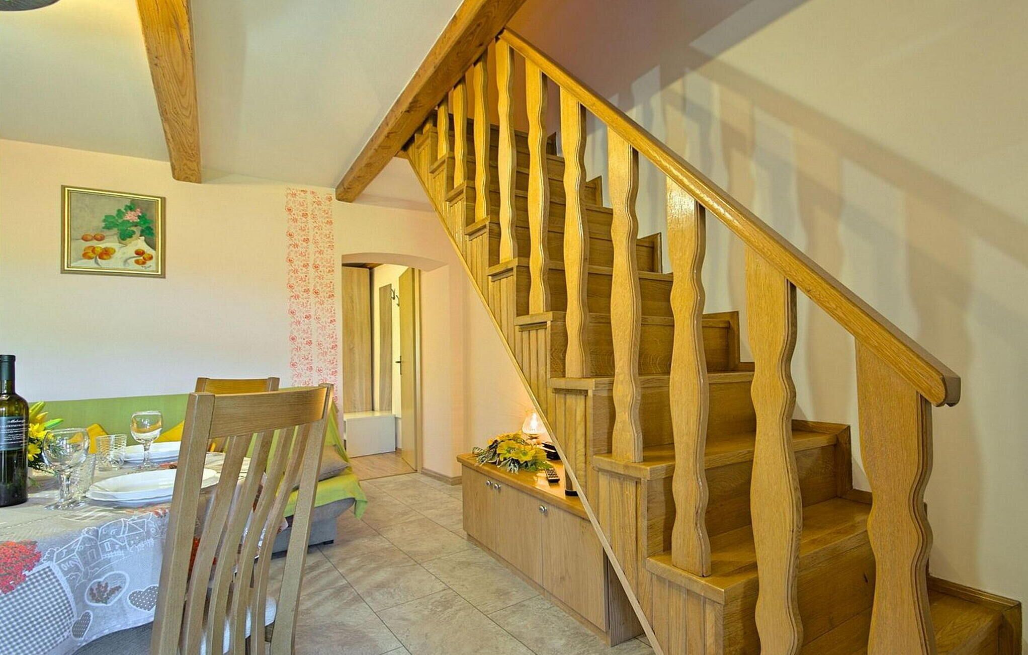 Un coin repas agrémenté d’un escalier en bois, d’une table dressée pour deux personnes et d’une décoration murale à motifs floraux.