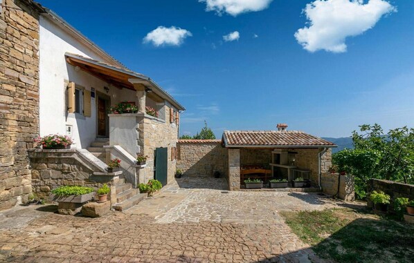 A stone building with a tiled roof, a stone staircase, and a small garden area with potted plants.