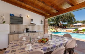 Ein Essbereich mit Blick auf den Pool, eine Küche mit modernen Geräten und eine rustikale Holzbalkendecke.
