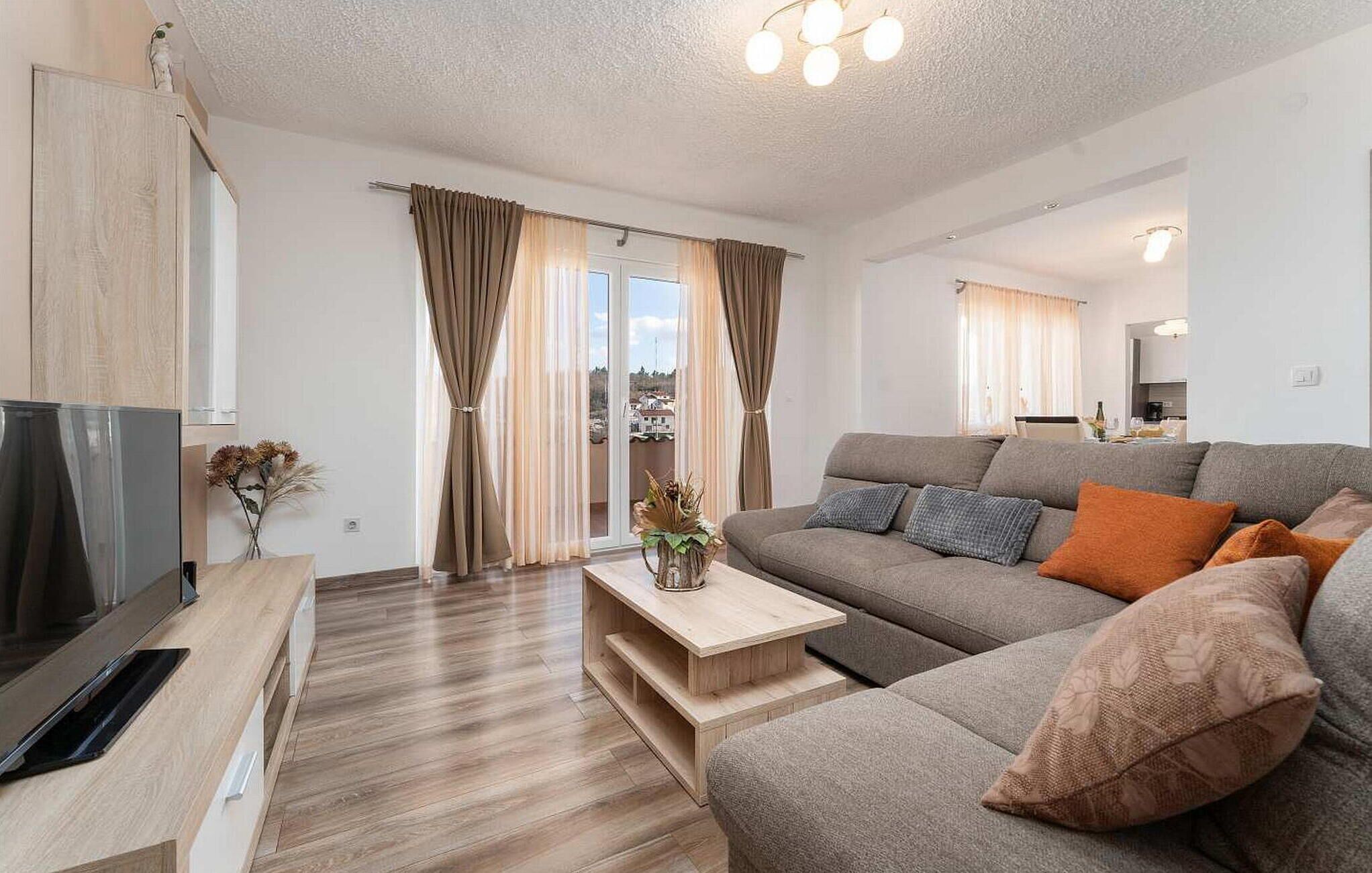 Een moderne woonkamer met een grijze bank, een houten salontafel en een flatscreen televisie op een houten dressoir.