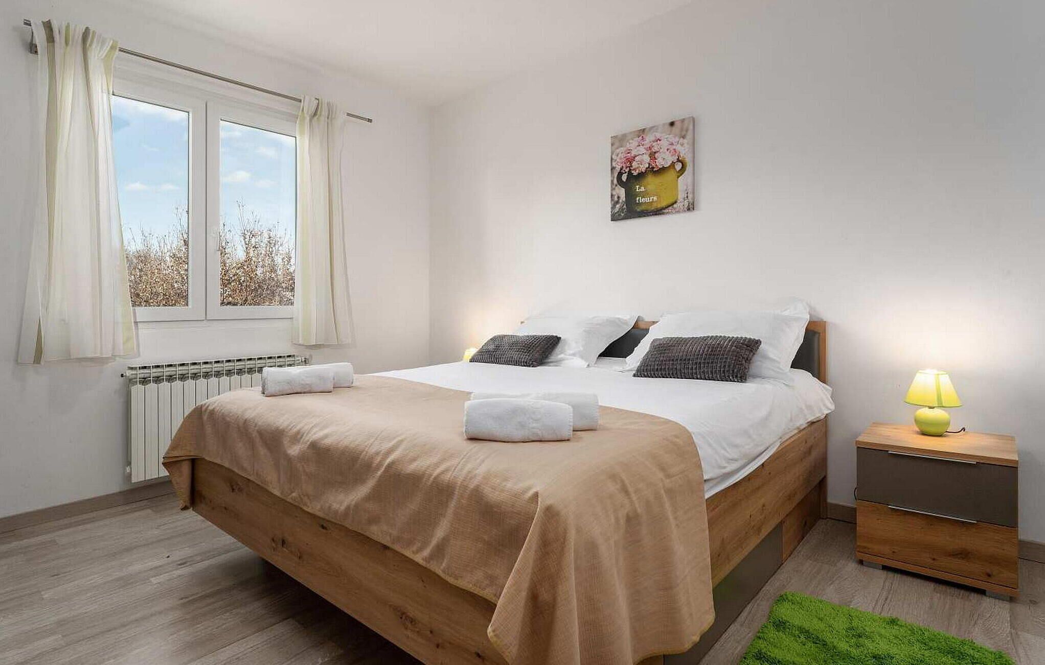 A bedroom with a bed, a nightstand, a lamp, a radiator, and a window with curtains.