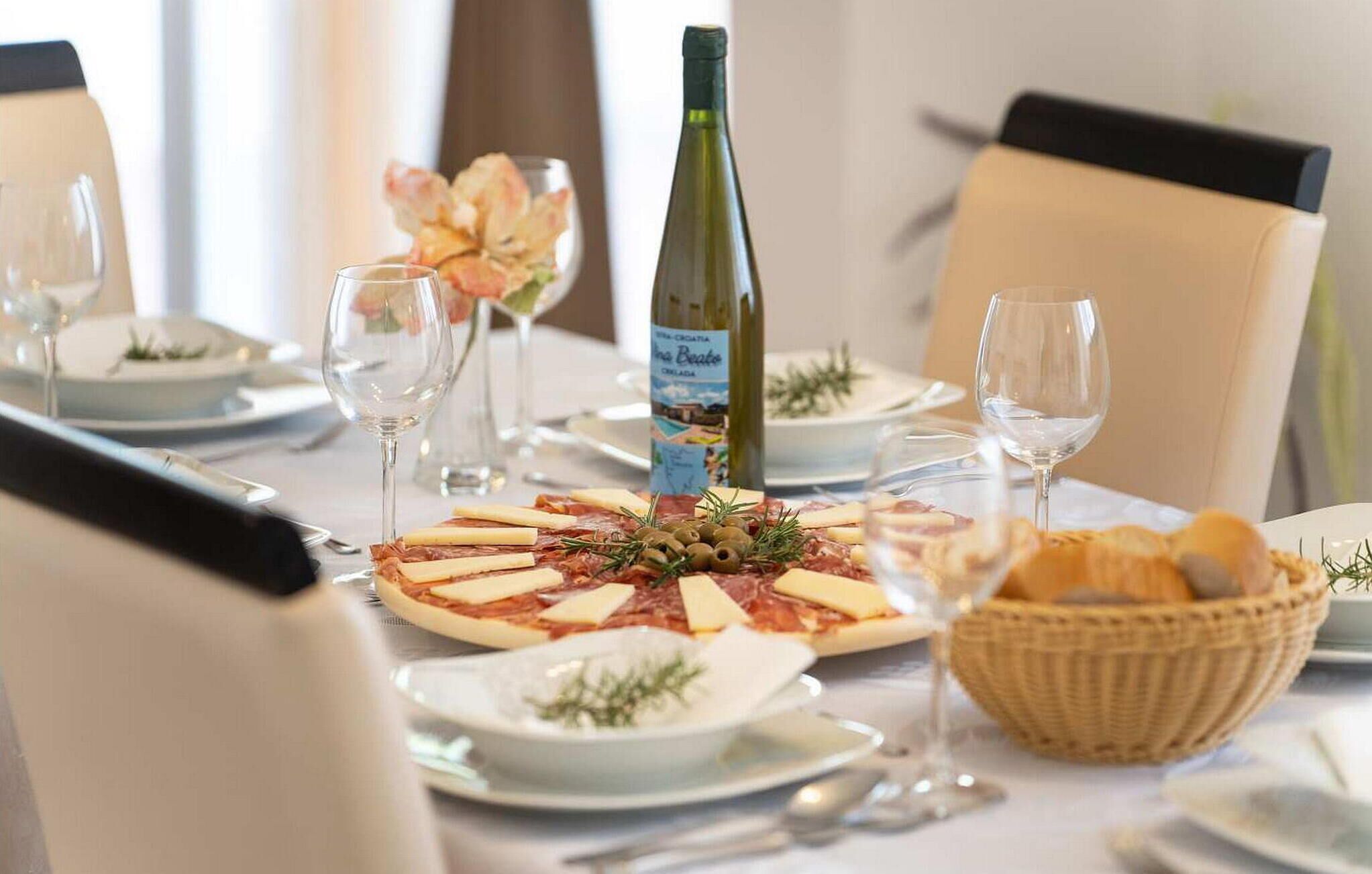 A dining table set with plates, glasses, a bottle of wine, and a pizza with cheese and olives.