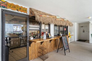 Um bar tiki com um telhado de palha, um balcão de madeira e um quadro de cardápio.