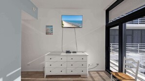 A modern room with a white dresser, a flat-screen TV mounted on the wall, and a large window offering a view of a balcony. - South Padre Resort Rentals - Sunchase IV #327 (South Padre Island)