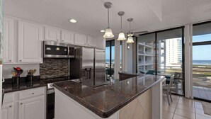 A modern kitchen with granite countertops, stainless steel appliances, and a view of the ocean through large sliding glass doors. - South Padre Resort Rentals - Sunchase IV #327 (South Padre Island)