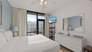 A hotel room with a large bed, a dresser, a mirror, and a view of the city through a large window. - South Padre Resort Rentals - Sunchase IV #327 (South Padre Island)