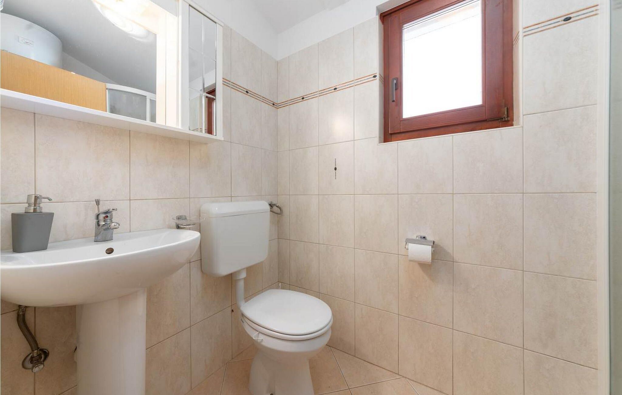 A bathroom with a white sink, toilet, and a window above the toilet.