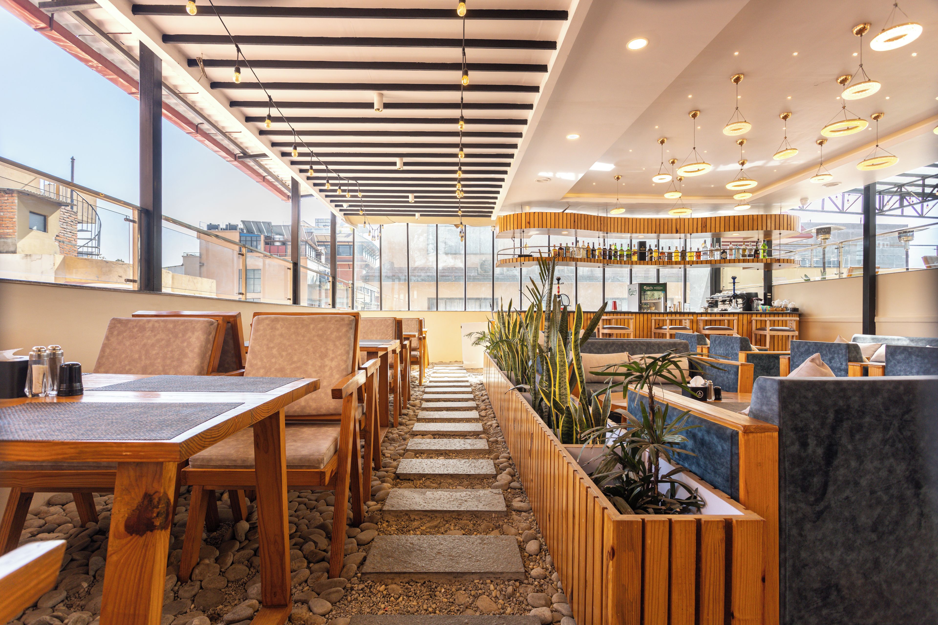Un restaurante moderno con mesas y sillas de madera, una zona de bar con botellas, y vistas amplias a través de grandes ventanales.