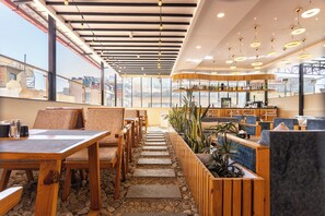 A modern restaurant with wooden tables and chairs, a bar area with bottles, and a view through large windows. - Kathmandu Business Hotel (Kathmandu)