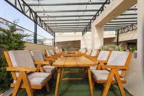 An outdoor seating area with wooden tables and chairs, a glass ceiling, and green artificial turf. - Kathmandu Business Hotel (Kathmandu)