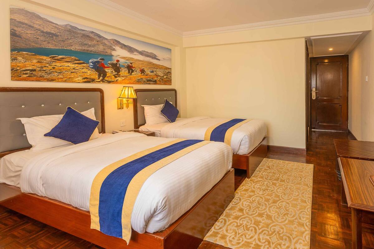 Une chambre d’hôtel avec deux lits, un grand tableau représentant un paysage montagneux, un plancher en bois et un bureau en bois.