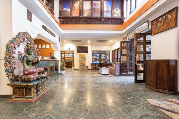 A spacious lobby with a reception desk, a Buddha statue, and a traditional wooden cabinet. - Kathmandu Business Hotel (Kathmandu)