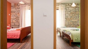 Une chambre avec deux lits, des murs en pierre, un plancher en bois et des luminaires suspendus.