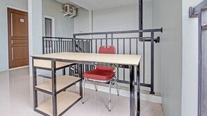 Una habitación con una mesa, una silla roja, una puerta de madera y una escalera con barandilla de metal.