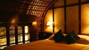 Quarto com cama, luminária e janela com vista para um muro de tijolos.