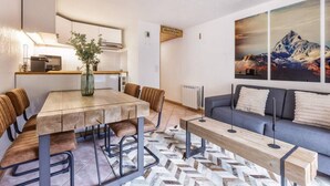 Una sala moderna con una mesa de comedor de madera, sillas de cuero, un sofá gris y un cuadro grande de montañas en la pared.