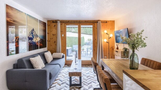 Una sala moderna con un sofá gris, una mesa de comedor de madera y piso con patrón de espiga.