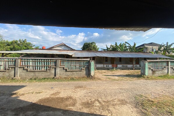 A building with a corrugated metal roof, a concrete wall with a metal railing, and a dirt ground.