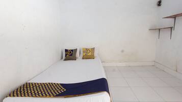 Quarto pequeno com uma cama de solteiro, colcha branca, duas almofadas estampadas e manta azul-marinho.