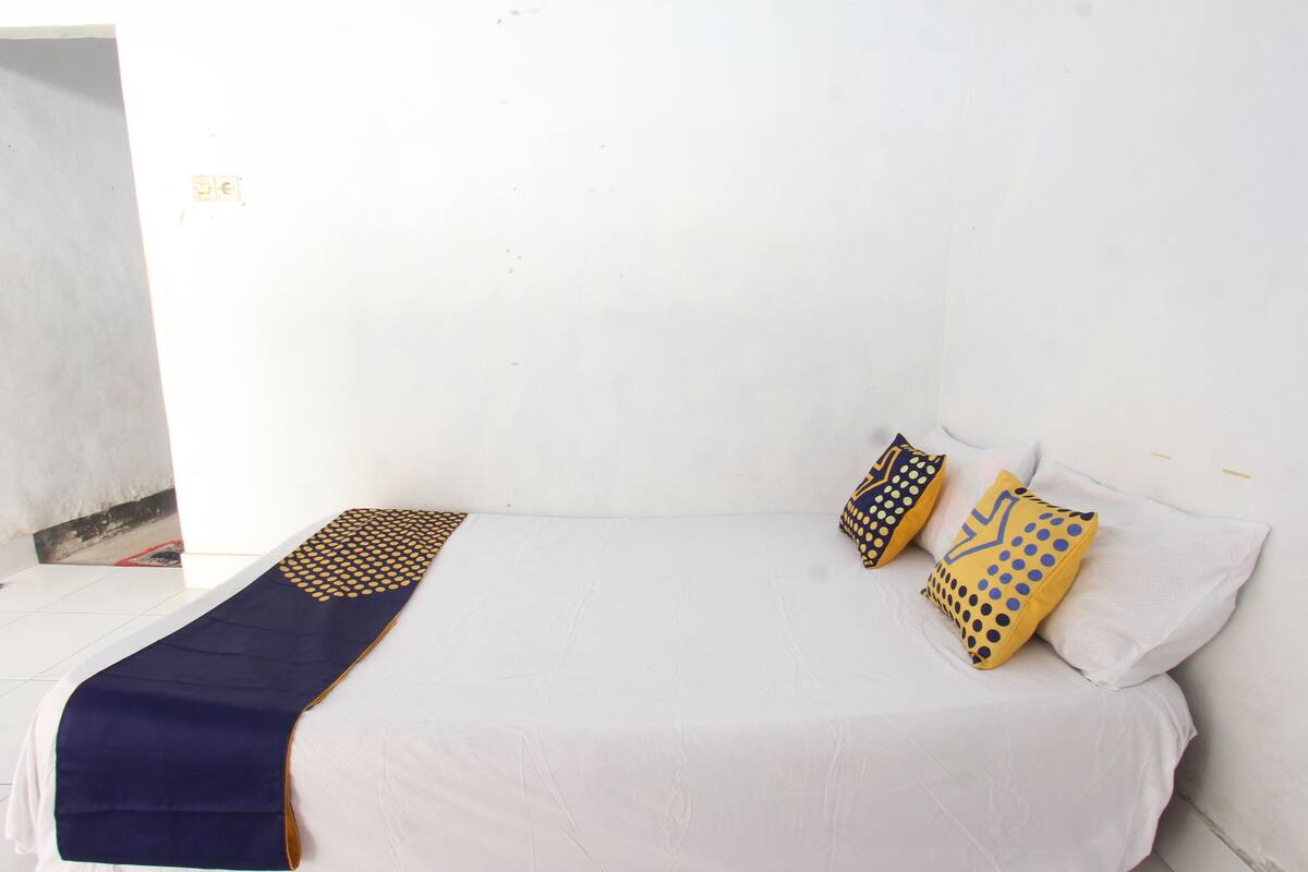A single-bed room with a white bedspread, a navy blue throw blanket, and two patterned pillows.