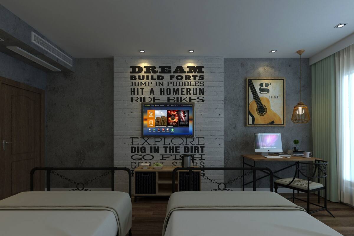 A hotel room with two beds, a desk with a computer, a TV mounted on the wall, and a guitar poster.