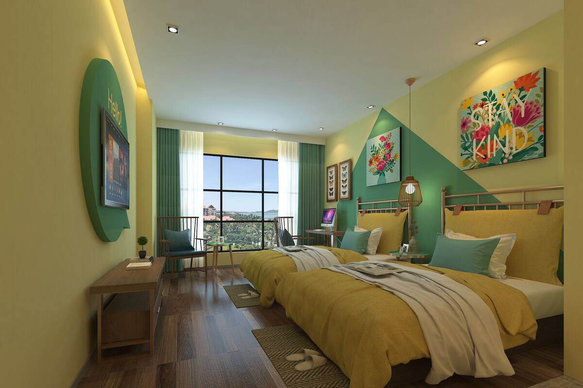 A modern hotel room with a large bed, a desk with a computer, a chair, and a view of the city through large windows.