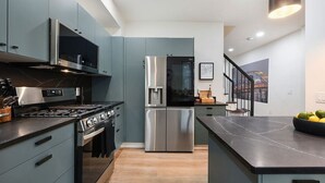 A modern kitchen with grey cabinets, stainless steel appliances, and a black countertop. - ★ HostWise Stays ★ Off-Street Parking, 2 Full Baths, Great Patio! (Pittsburgh)
