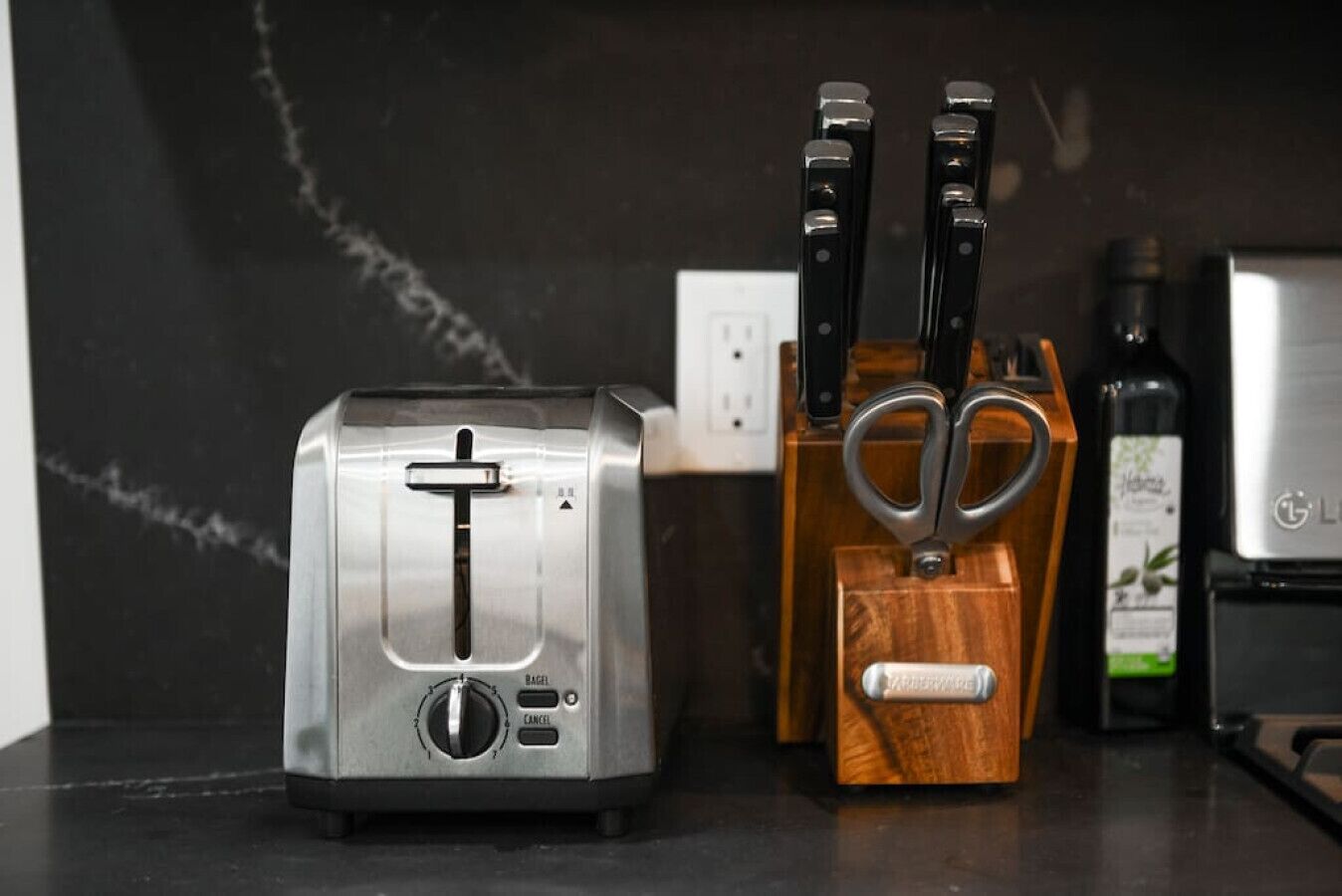 A kitchen counter with a toaster, a knife block, and a bottle of olive oil.